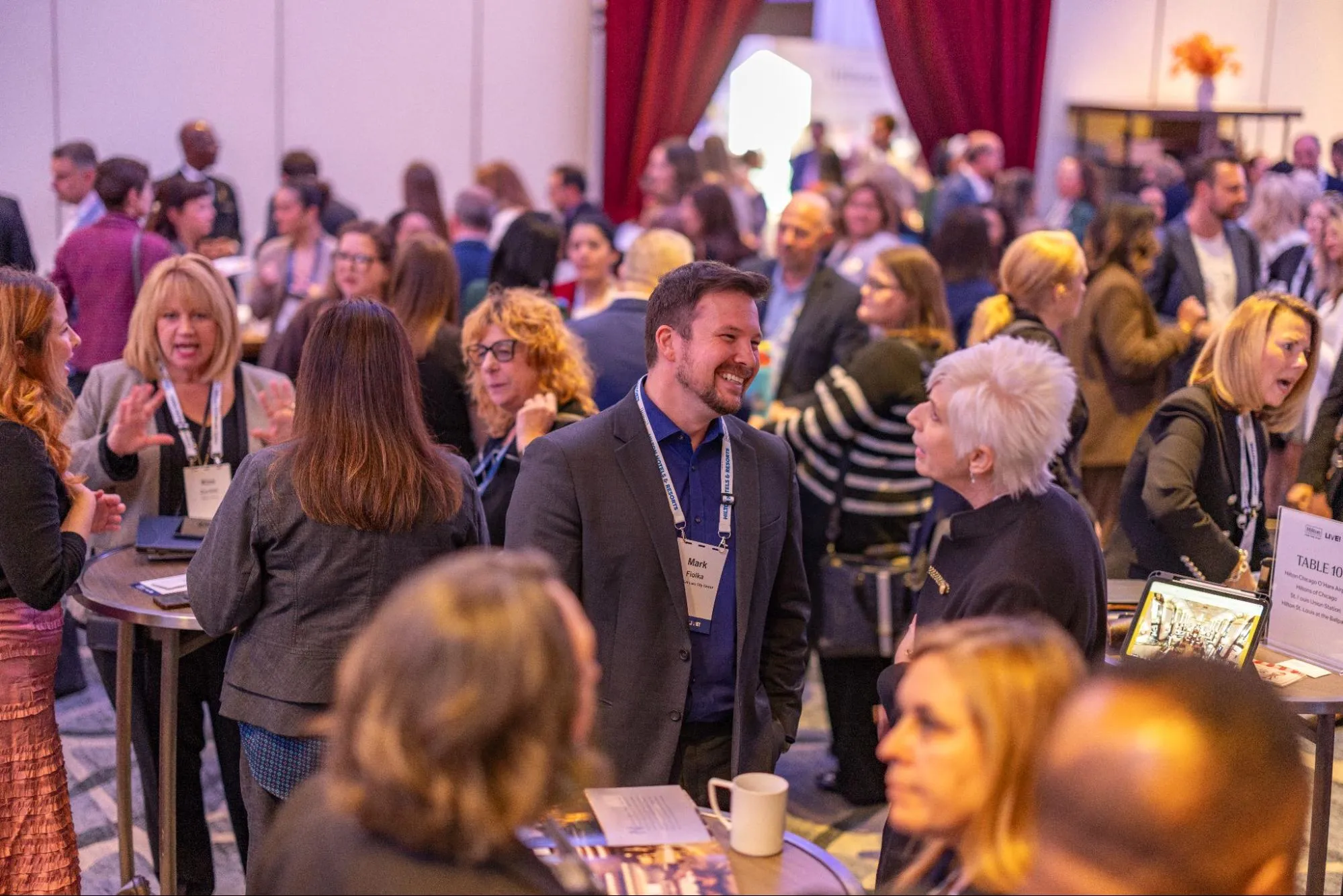 Conference attendees in business casual attire stand in small groups, smiling and talking
